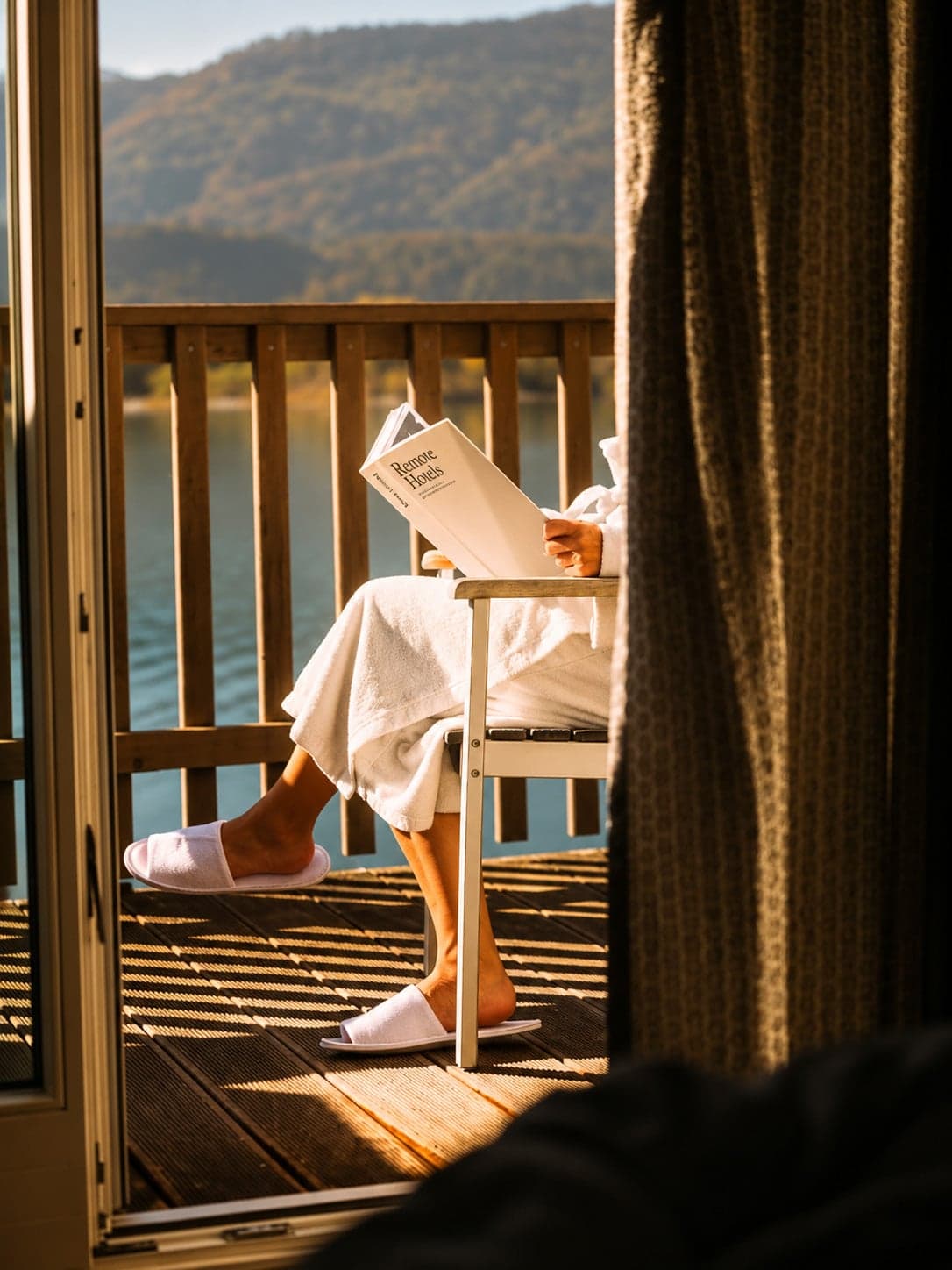 Someone in a white robe reading on a sunny balcony