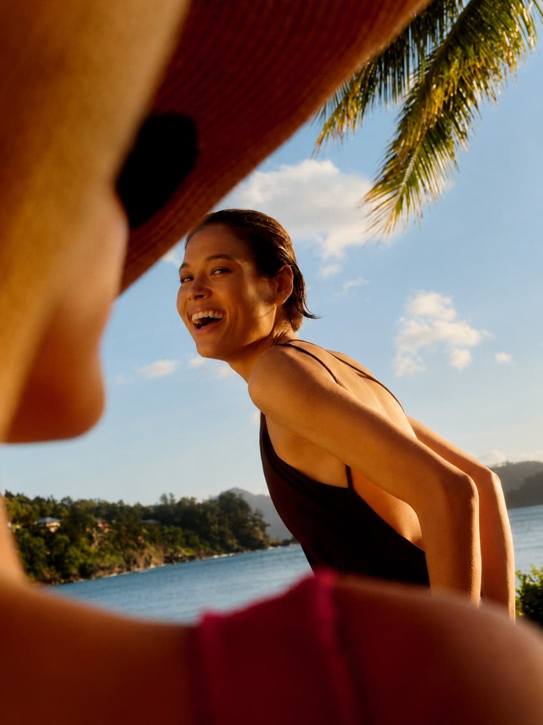 A woman laughing on the beach, framed by a straw hat brim