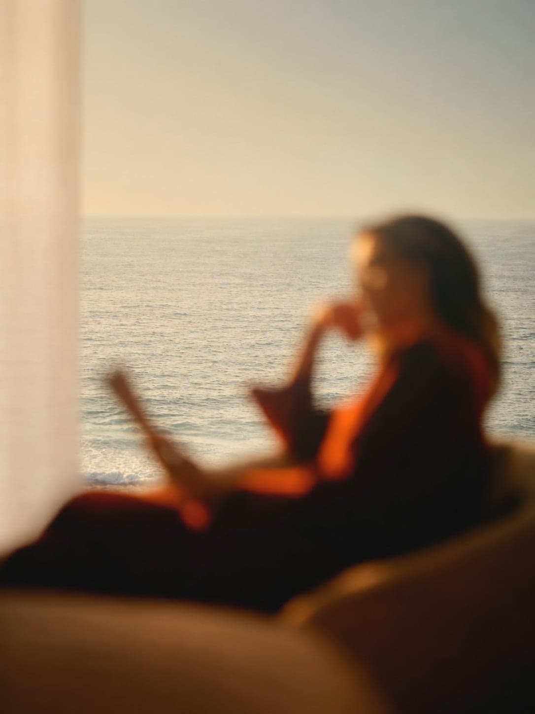 A woman by a window overlooking the sea, softly out of focus